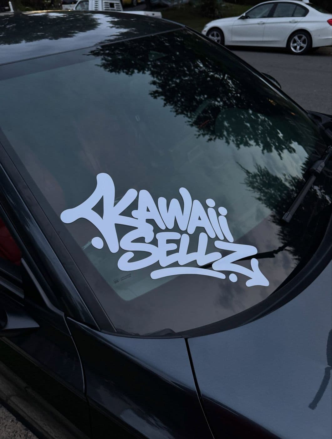 White graffiti-style “Kawaii Sellz” decal on a black car’s windshield