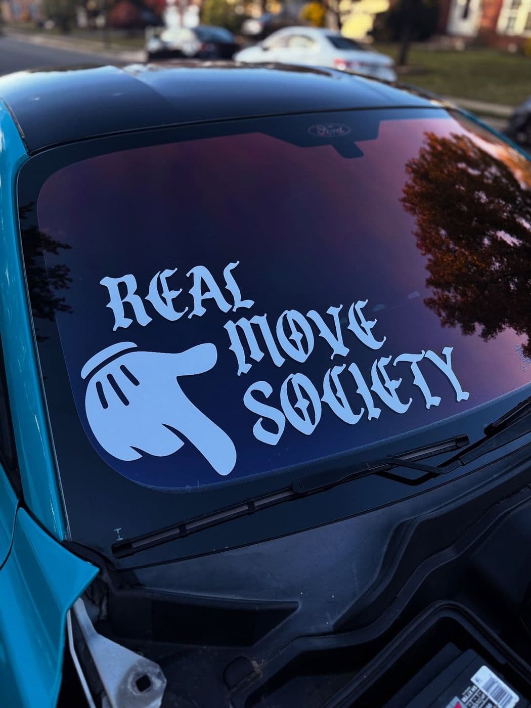 White “Real Move Society” windshield banner with a hand graphic on a blue car