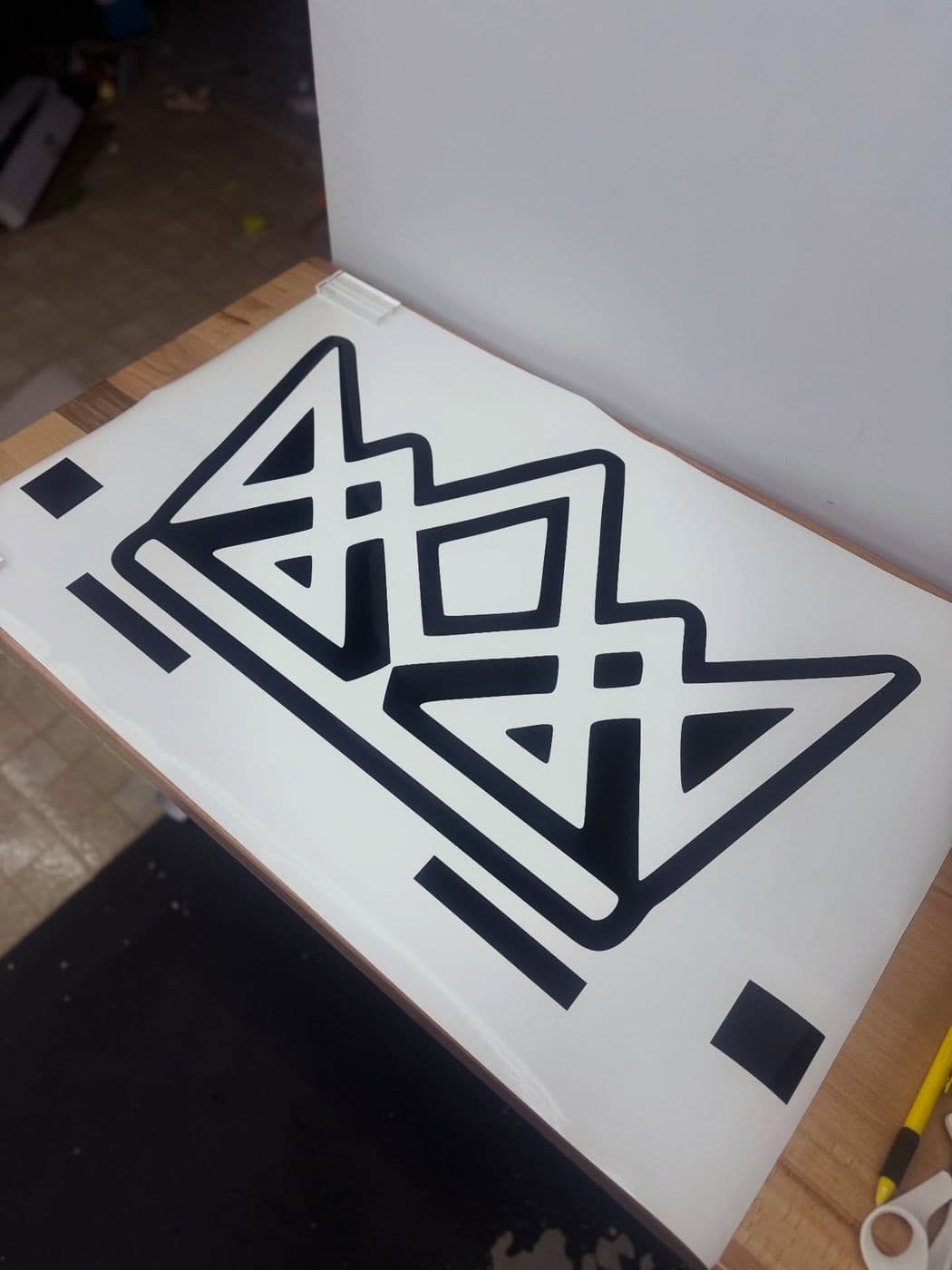 Large black geometric logo decal being weeded from gloss black vinyl on a white backing sheet