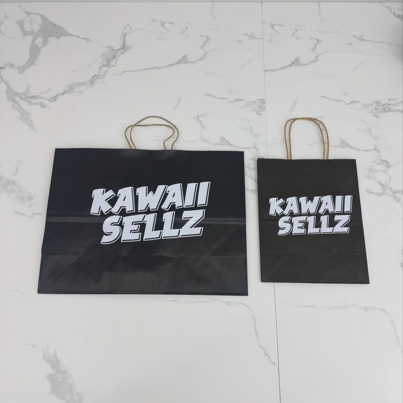 Black paper shopping bags printed with a white “Kawaii Sellz” logo