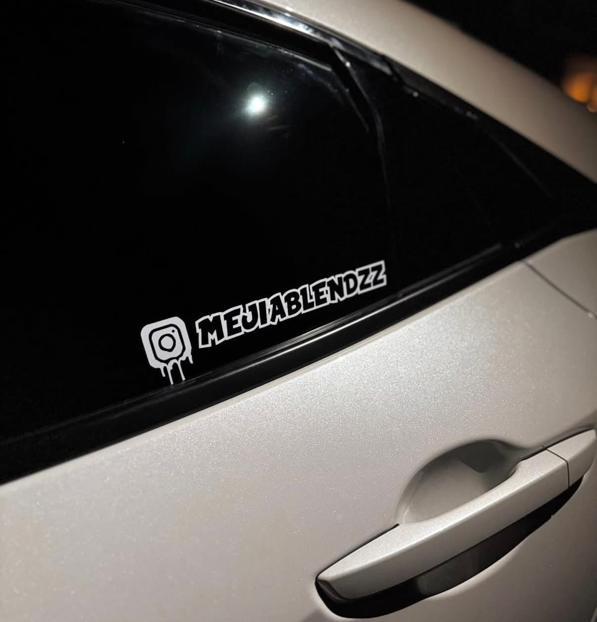 White Instagram MEJIABLENDZZ drip decal on the rear side window of a white car